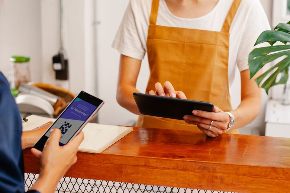 Une personne tient un smartphone devant un comptoir, face à une tablette, photo d’illustration.