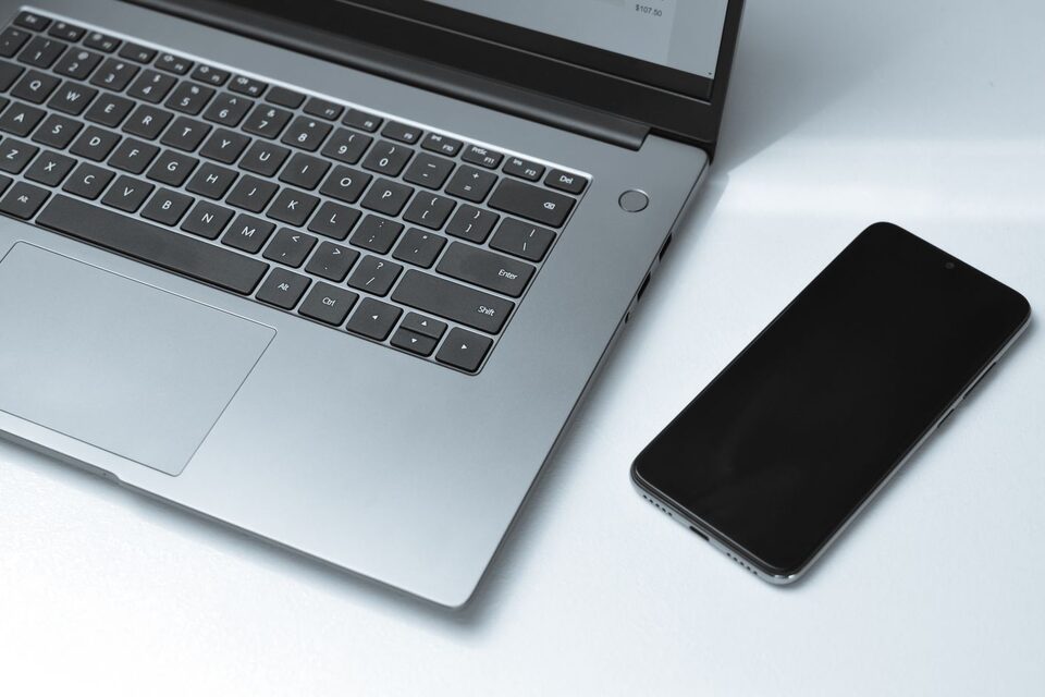 Un ordinateur portable et un téléphone à écran noir sur un bureau blanc, photo d’illustration.