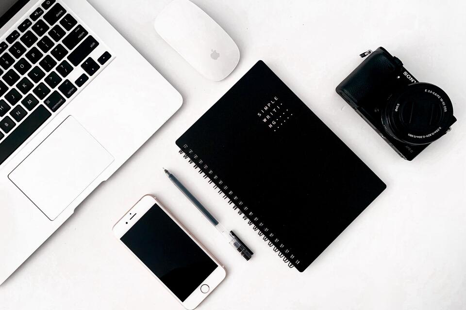 Een laptop, telefoon en notitieboek op een wit bureau, illustratieve foto.