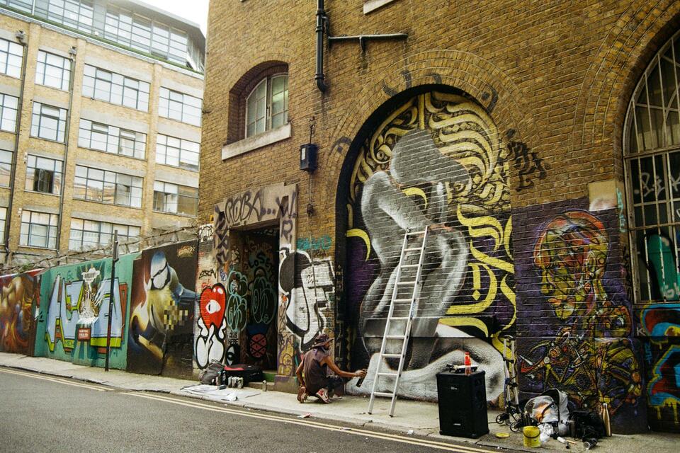 An artist works below walls covered in street art on Brick Lane, illustrative photograph.