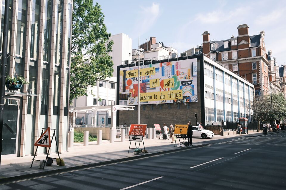 Een groot kleurrijk reclamebord staat boven het trottoir van een stadsstraat.