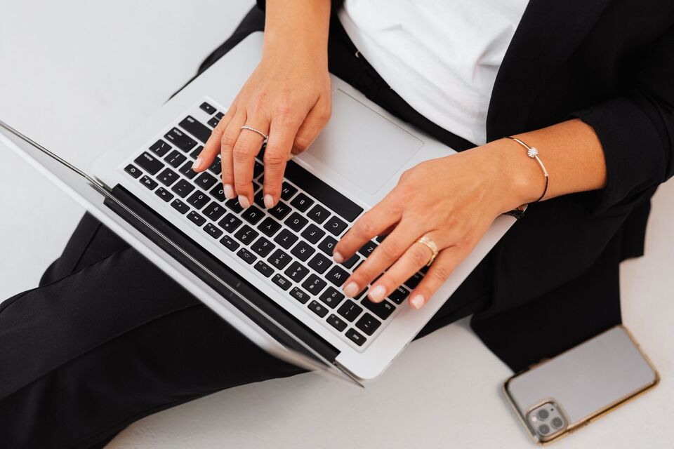 A person types on a laptop with a phone placed beside them.