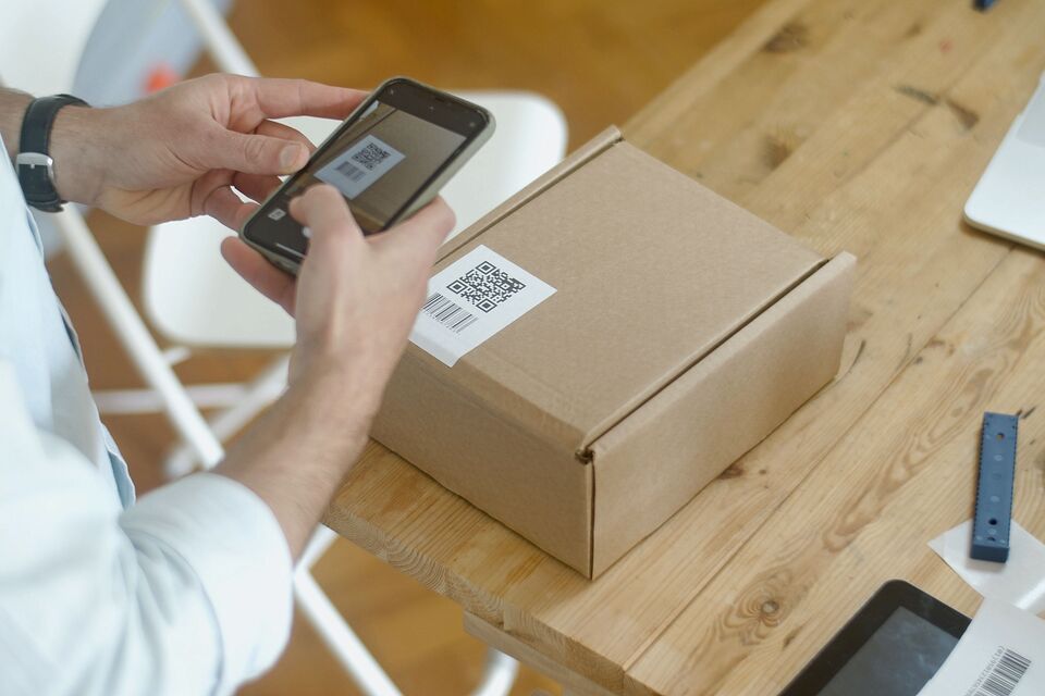 Une personne cadre avec son téléphone le QR code collé sur une boîte.