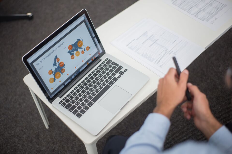 A person reviews documents beside a laptop displaying charts.