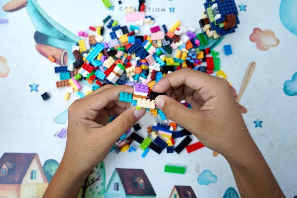 Des mains assemblent des briques en plastique colorées sur une table, photo d’illustration.