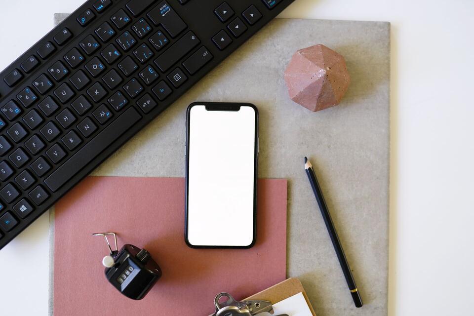 Een telefoon met een leeg scherm naast een toetsenbord en kantoorbenodigdheden, illustratieve foto.