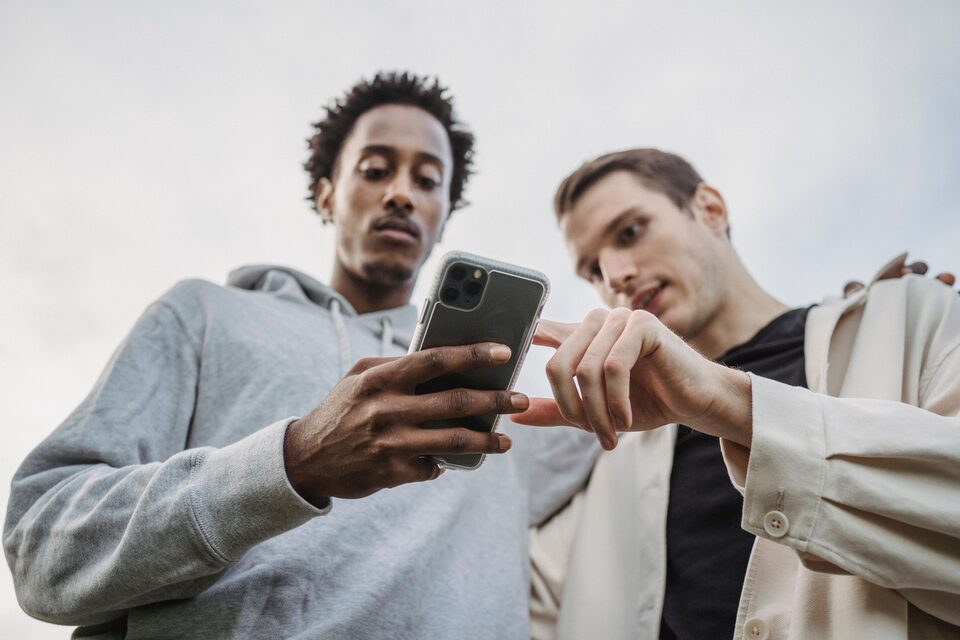 Deux personnes regardent ensemble un smartphone à l’extérieur, photo d’illustration.