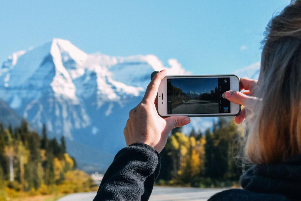 Une personne photographie des montagnes enneigées avec un téléphone, photo d’illustration.
