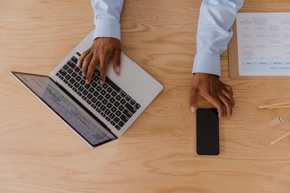Handen gebruiken een laptop en een telefoon op een bureau, illustratieve foto.